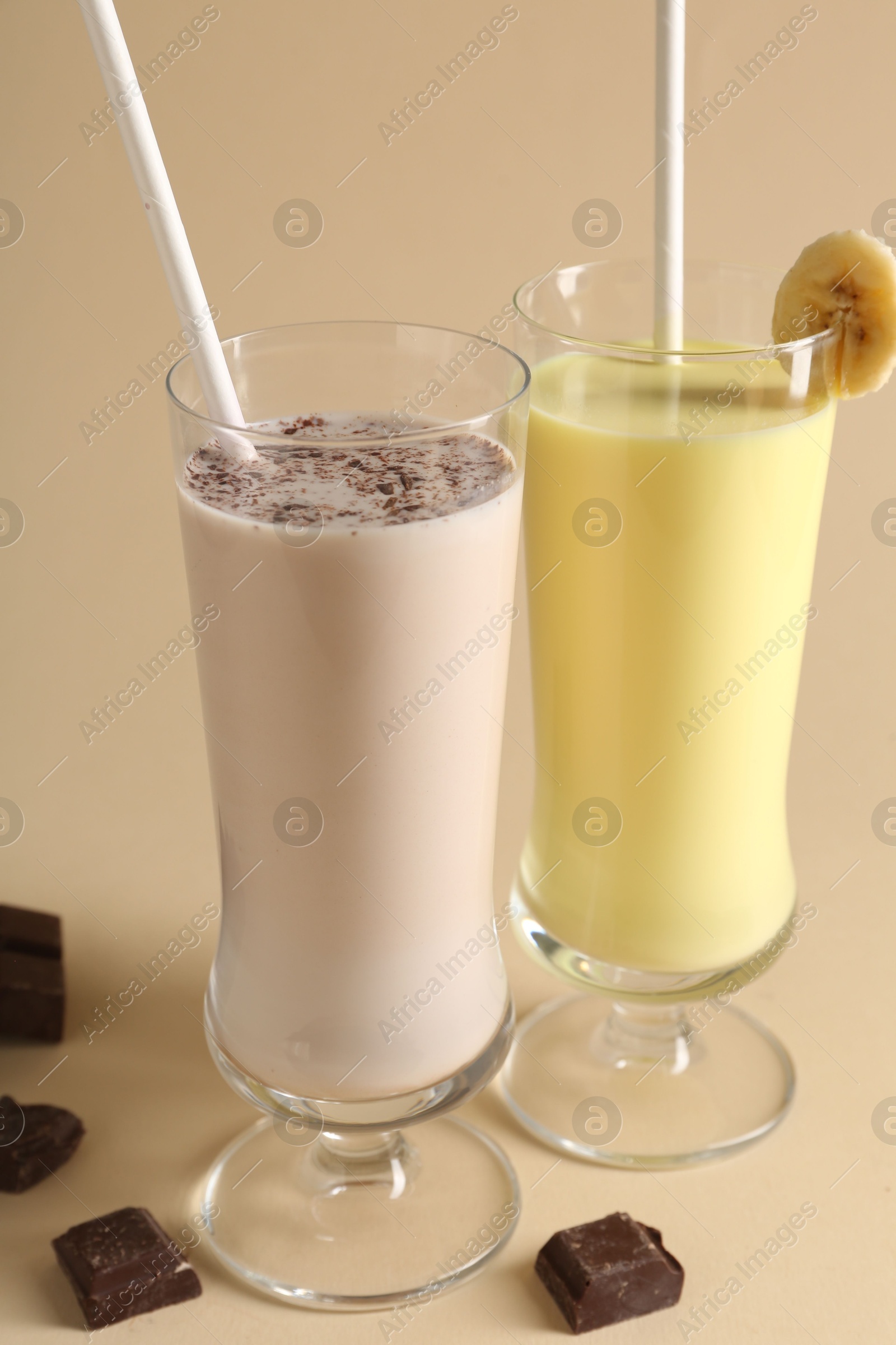 Photo of Different tasty milkshakes in glasses and pieces of chocolate on beige background, closeup