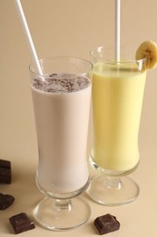 Photo of Different tasty milkshakes in glasses and pieces of chocolate on beige background, closeup