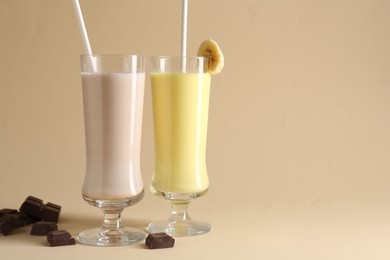 Photo of Different tasty milkshakes in glasses and pieces of chocolate on beige background, space for text