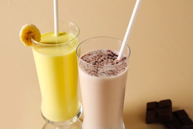Photo of Different tasty milkshakes in glasses and pieces of chocolate on beige background, closeup