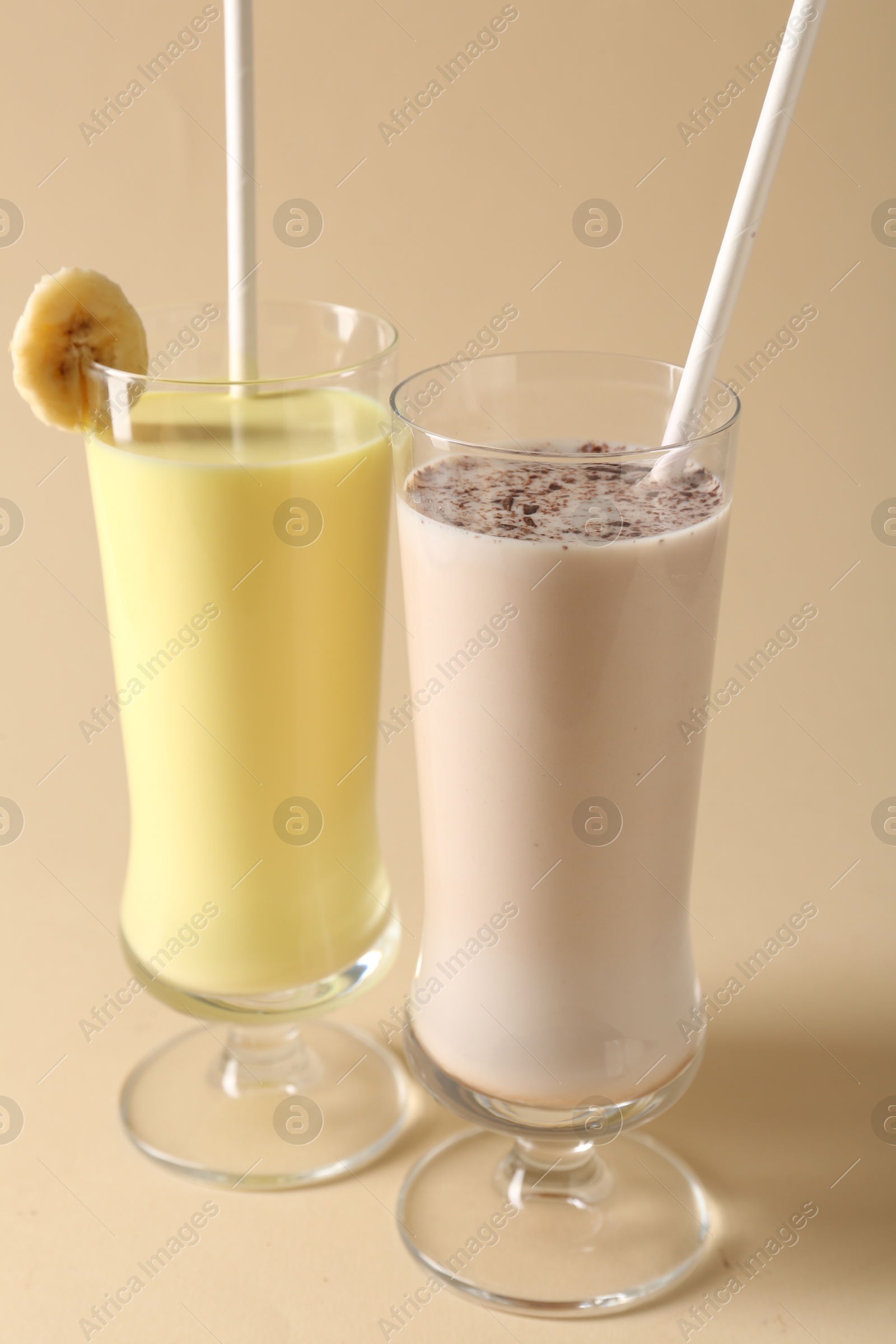 Photo of Different tasty milkshakes in glasses on beige background, closeup