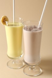 Photo of Different tasty milkshakes in glasses on beige background, closeup