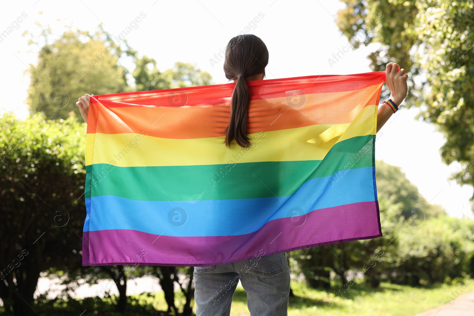 LGBT concept. Woman with rainbow flag outdoors, back view Photo of LGBT concept. Woman with rainbow flag outdoors, back view