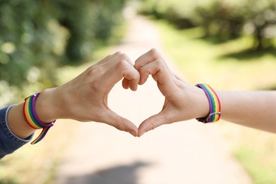 Photo of LGBT concept. Women in rainbow wristbands making heart shape outdoors, closeup