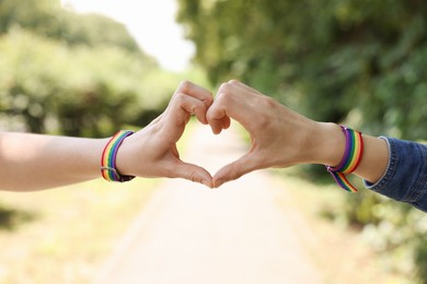 Photo of LGBT concept. Women in rainbow wristbands making heart shape outdoors, closeup