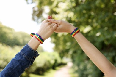 Photo of LGBT concept. Women in rainbow wristbands holding hands outdoors, closeup