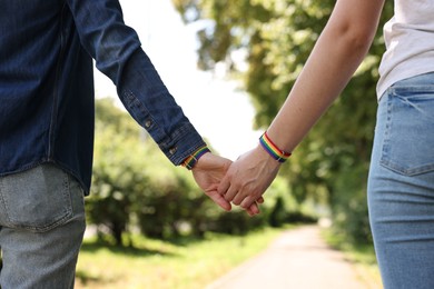 Photo of LGBT concept. Women in rainbow wristbands holding hands outdoors, closeup
