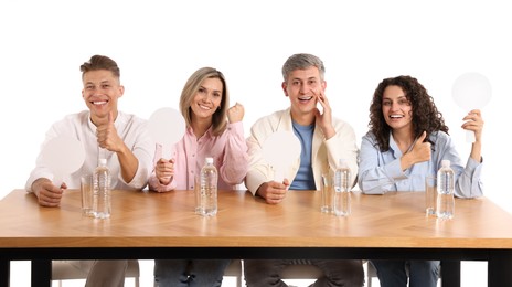 Photo of Panel of happy judges with blank score signs at table on white background