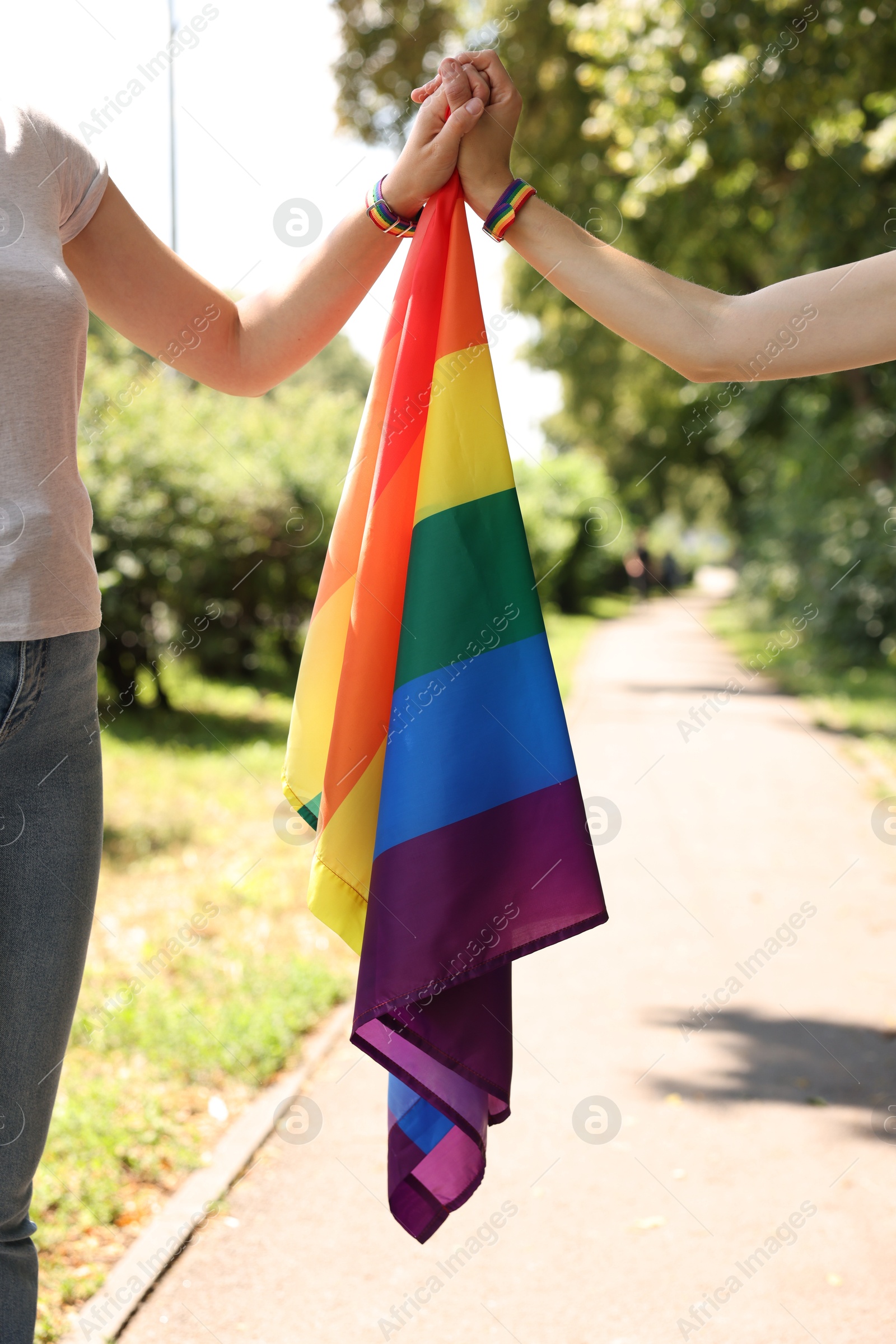 Photo of LGBT concept. Women with rainbow flag holding hands outdoors, closeup