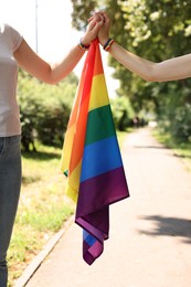 Photo of LGBT concept. Women with rainbow flag holding hands outdoors, closeup