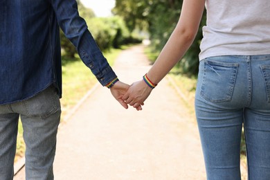 Photo of LGBT concept. Women in rainbow wristbands holding hands outdoors, closeup