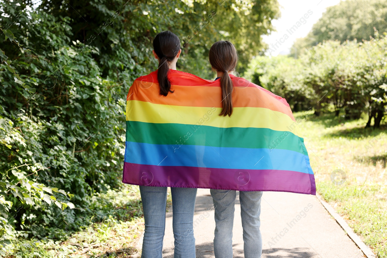 LGBT concept. Women with rainbow flag outdoors, back view Photo of LGBT concept. Women with rainbow flag outdoors, back view
