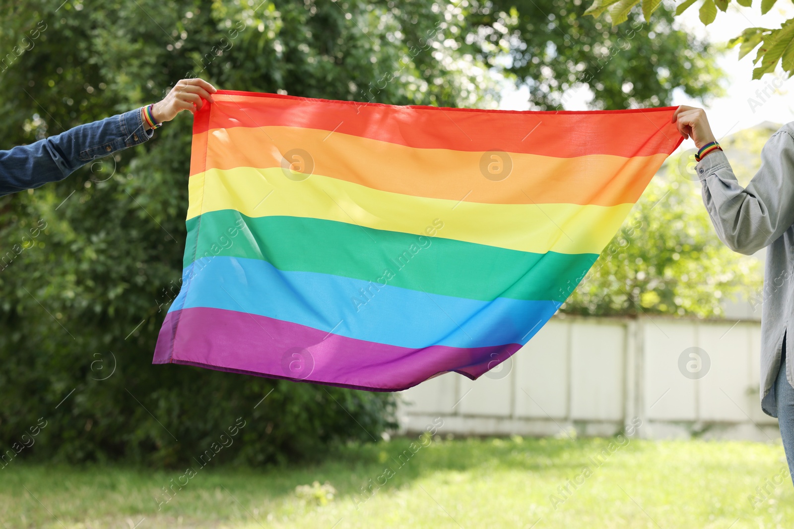 LGBT concept. Women in wristbands with rainbow flag outdoors, closeup Photo of LGBT concept. Women in wristbands with rainbow flag outdoors, closeup