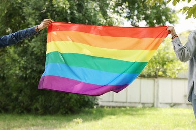 Photo of LGBT concept. Women in wristbands with rainbow flag outdoors, closeup