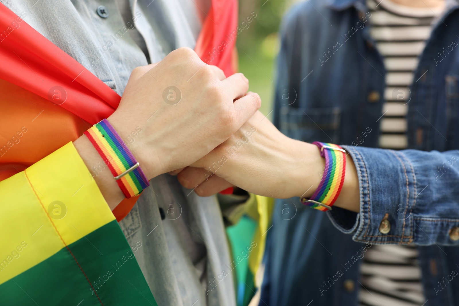 LGBT concept. Women in rainbow wristbands holding hands outdoors, closeup Photo of LGBT concept. Women in rainbow wristbands holding hands outdoors, closeup