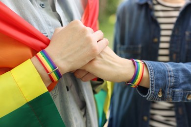 Photo of LGBT concept. Women in rainbow wristbands holding hands outdoors, closeup