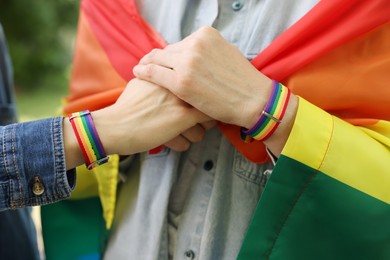 Photo of LGBT concept. Women in rainbow wristbands holding hands outdoors, closeup