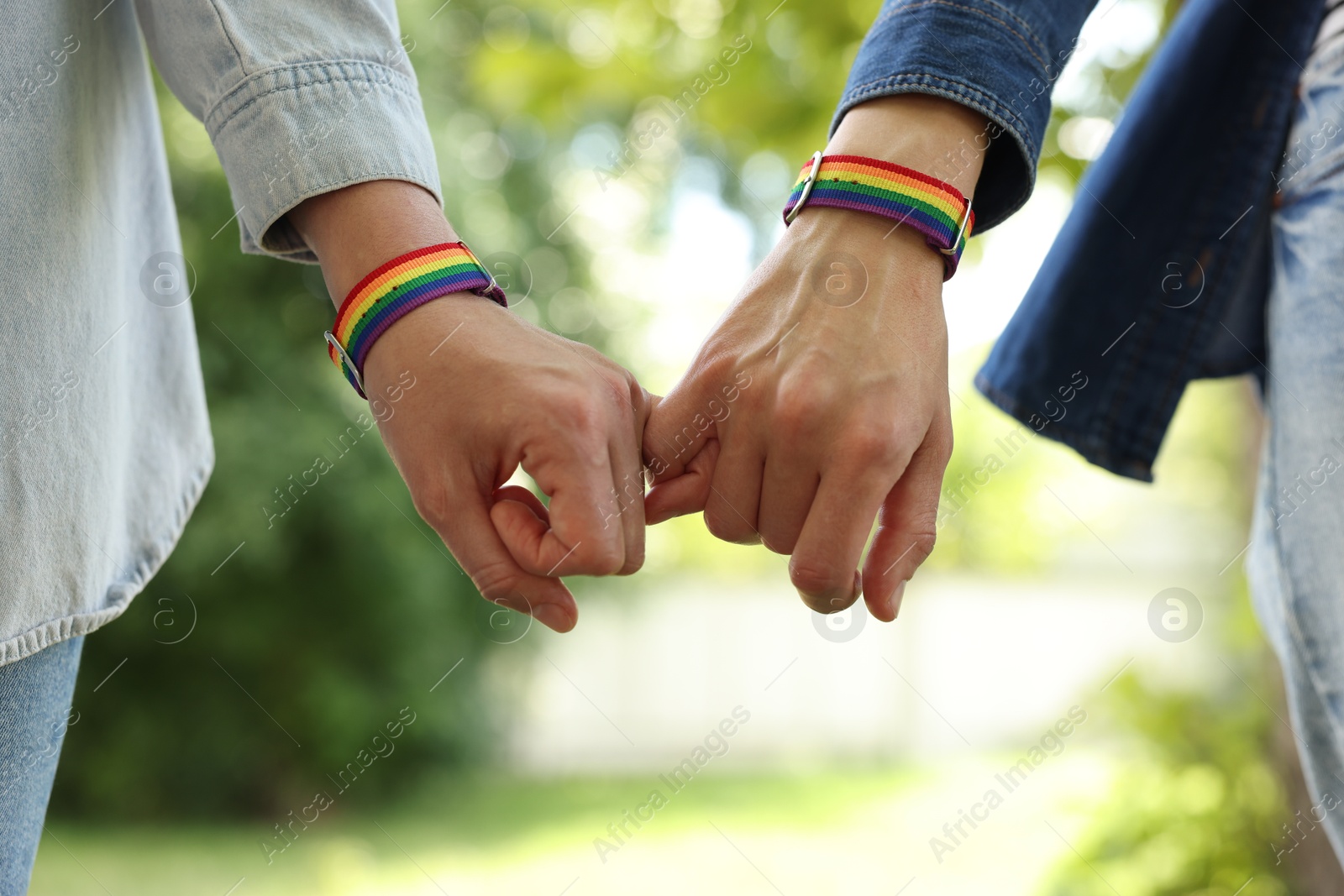 LGBT concept. Women in rainbow wristbands holding hands outdoors, closeup Photo of LGBT concept. Women in rainbow wristbands holding hands outdoors, closeup