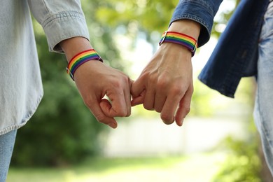 Photo of LGBT concept. Women in rainbow wristbands holding hands outdoors, closeup