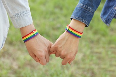 Photo of LGBT concept. Women in rainbow wristbands holding hands outdoors, closeup