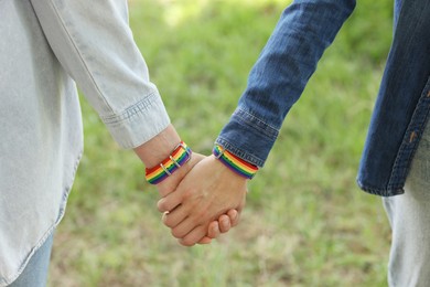 Photo of LGBT concept. Women in rainbow wristbands holding hands outdoors, closeup