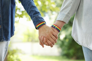 Photo of LGBT concept. Women in rainbow wristbands holding hands outdoors, closeup