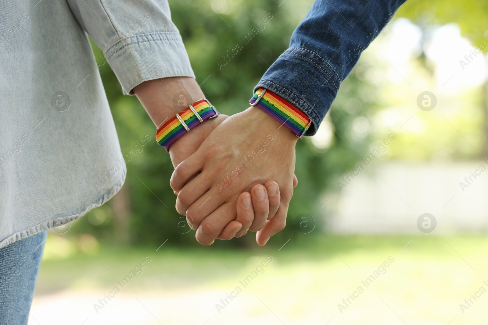 LGBT concept. Women in rainbow wristbands holding hands outdoors, closeup Photo of LGBT concept. Women in rainbow wristbands holding hands outdoors, closeup