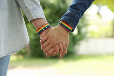 Photo of LGBT concept. Women in rainbow wristbands holding hands outdoors, closeup