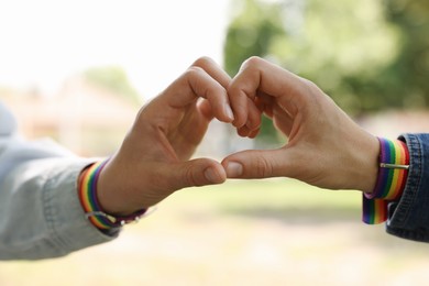 Photo of LGBT concept. Women in rainbow wristbands making heart shape outdoors, closeup