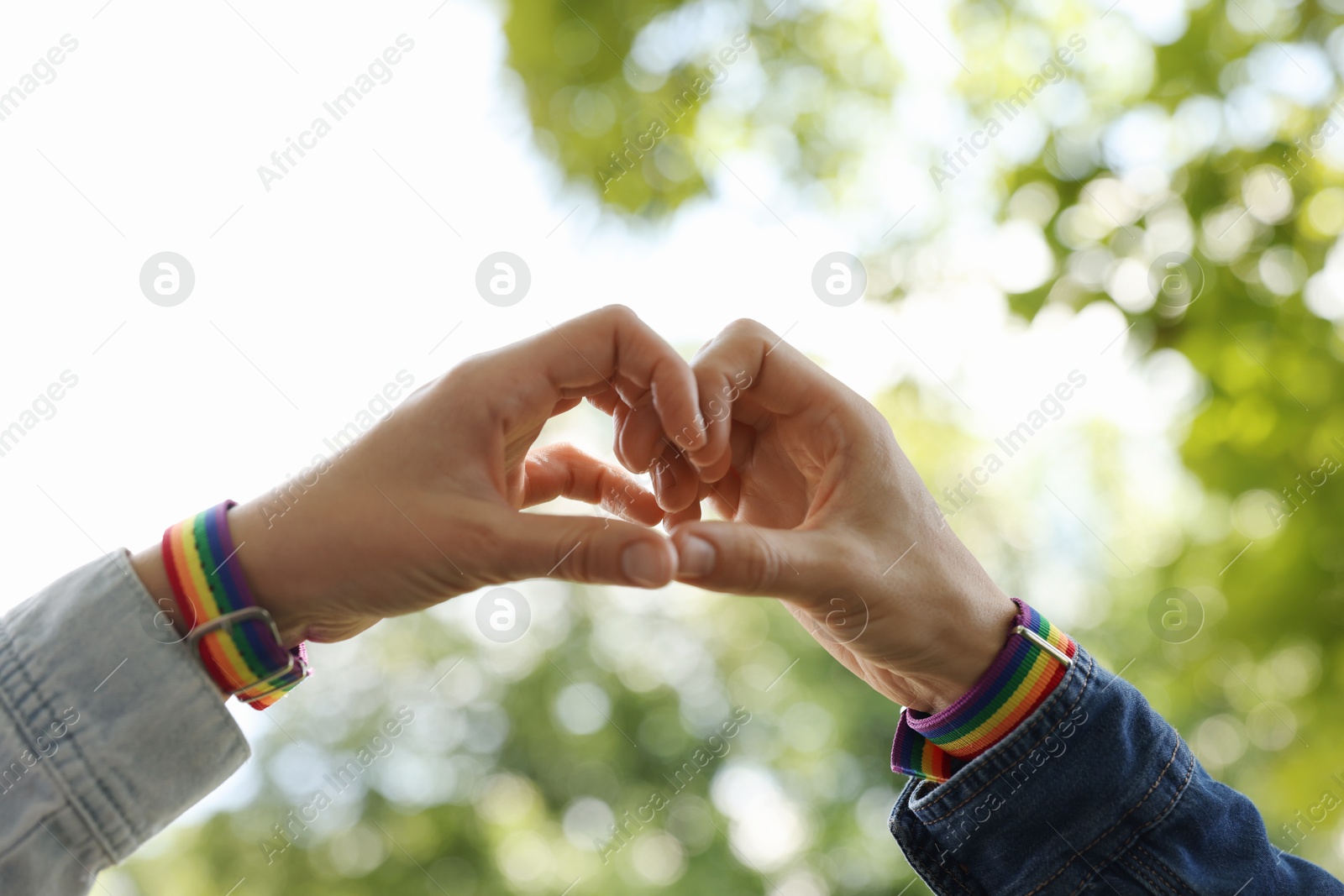 LGBT concept. Women in rainbow wristbands making heart shape outdoors, closeup Photo of LGBT concept. Women in rainbow wristbands making heart shape outdoors, closeup