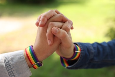 Photo of LGBT concept. Women in rainbow wristbands holding hands outdoors, closeup