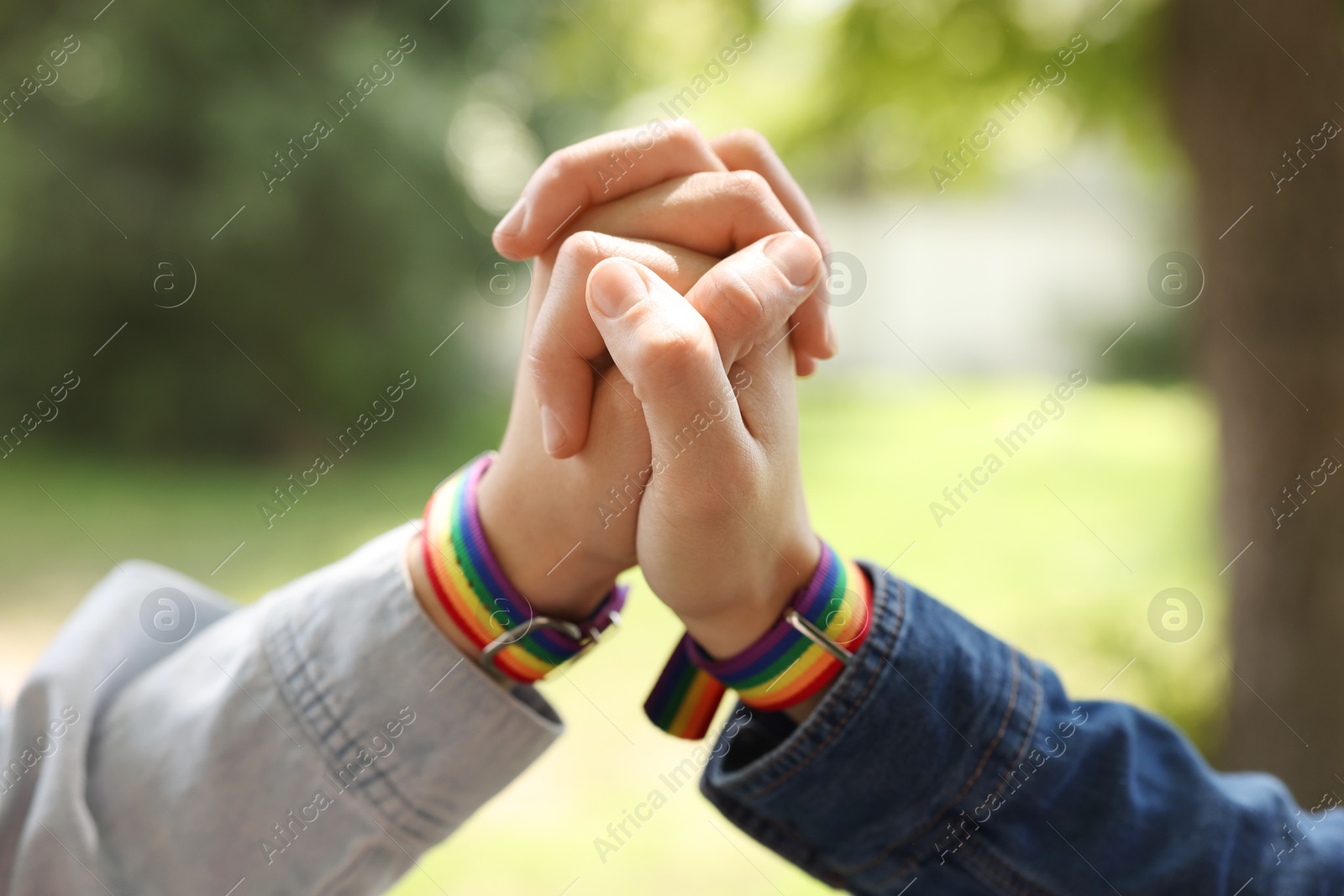 LGBT concept. Women in rainbow wristbands holding hands outdoors, closeup Photo of LGBT concept. Women in rainbow wristbands holding hands outdoors, closeup