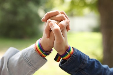Photo of LGBT concept. Women in rainbow wristbands holding hands outdoors, closeup