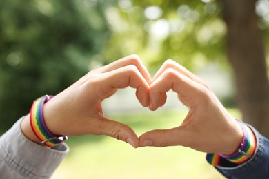 Photo of LGBT concept. Women in rainbow wristbands making heart shape outdoors, closeup