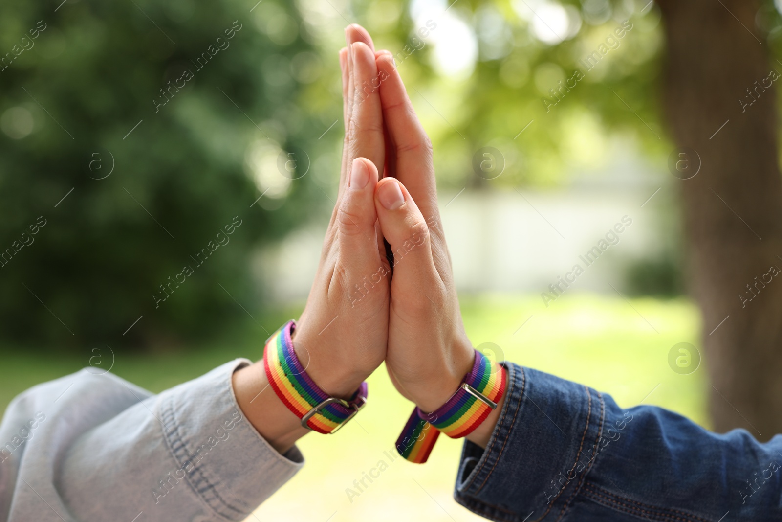 LGBT concept. Women in rainbow wristbands holding hands outdoors, closeup Photo of LGBT concept. Women in rainbow wristbands holding hands outdoors, closeup