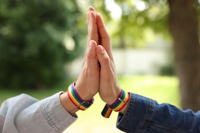 Photo of LGBT concept. Women in rainbow wristbands holding hands outdoors, closeup