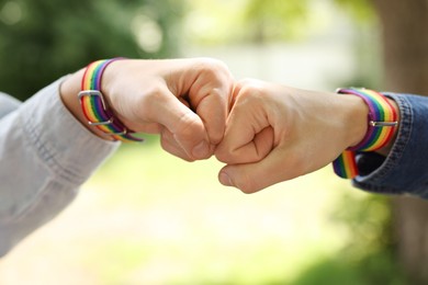 Photo of LGBT concept. Women in rainbow wristbands holding fists together outdoors, closeup