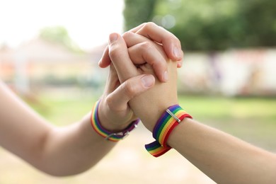 Photo of LGBT concept. Women in rainbow wristbands holding hands outdoors, closeup