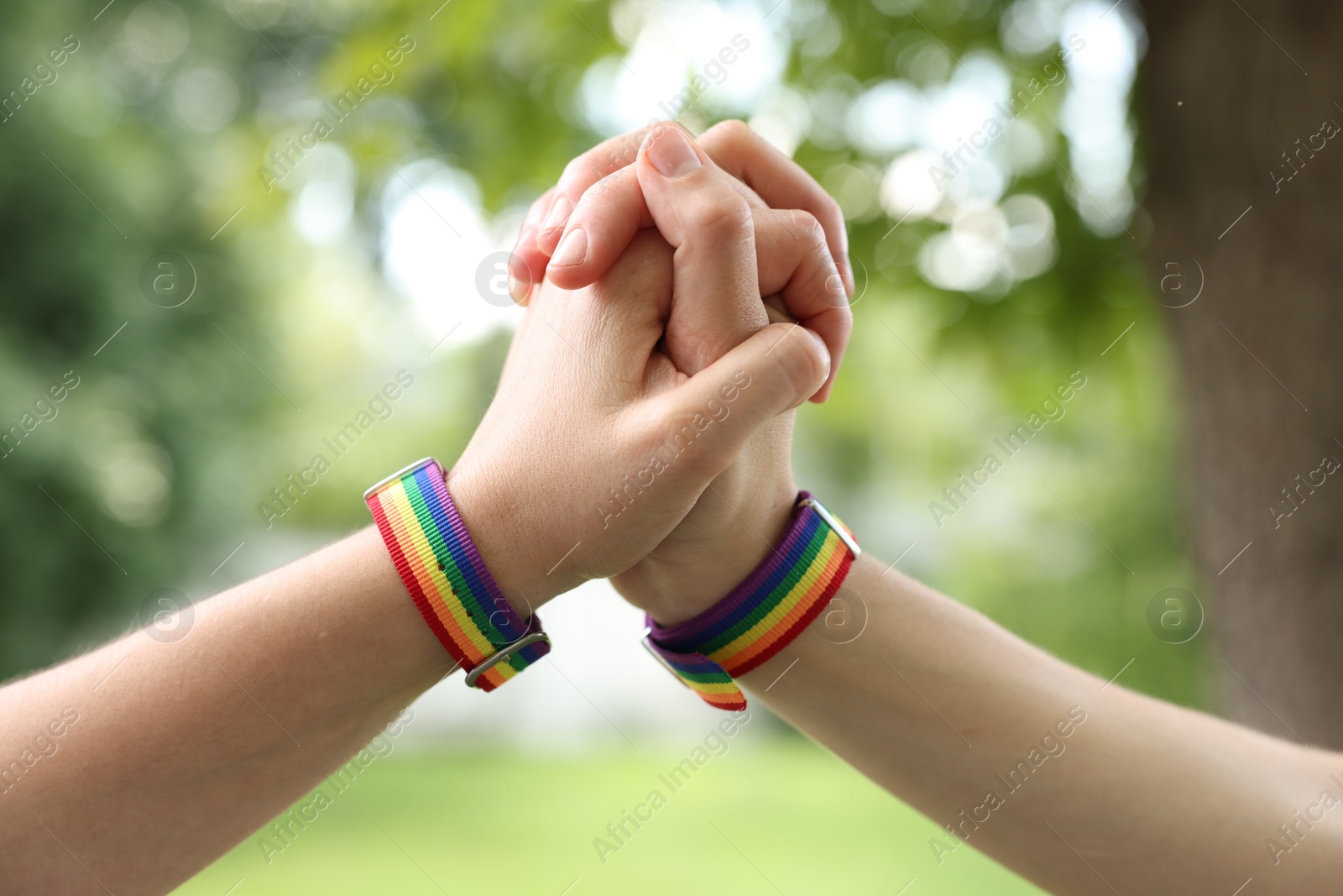 LGBT concept. Women in rainbow wristbands holding hands outdoors, closeup Photo of LGBT concept. Women in rainbow wristbands holding hands outdoors, closeup