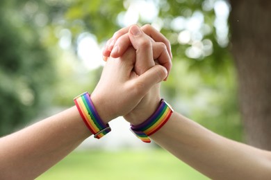 Photo of LGBT concept. Women in rainbow wristbands holding hands outdoors, closeup
