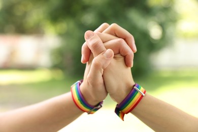 Photo of LGBT concept. Women in rainbow wristbands holding hands outdoors, closeup