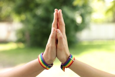 Photo of LGBT concept. Women in rainbow wristbands holding hands outdoors, closeup