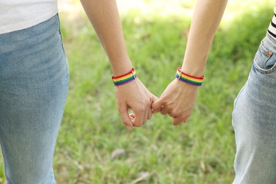 Photo of LGBT concept. Women in rainbow wristbands holding hands outdoors, closeup