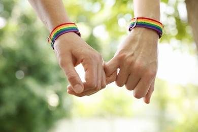Photo of LGBT concept. Women in rainbow wristbands holding hands outdoors, closeup