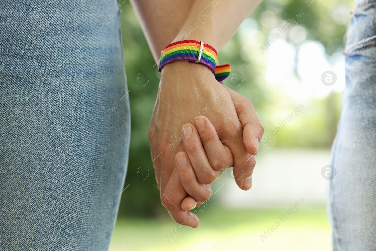 Photo of LGBT concept. Women in rainbow wristbands holding hands outdoors, closeup