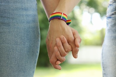 Photo of LGBT concept. Women in rainbow wristbands holding hands outdoors, closeup