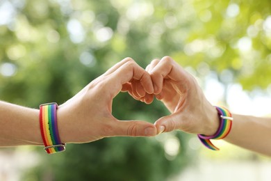 Photo of LGBT concept. Women in rainbow wristbands making heart shape outdoors, closeup