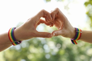 Photo of LGBT concept. Women in rainbow wristbands making heart shape outdoors, closeup