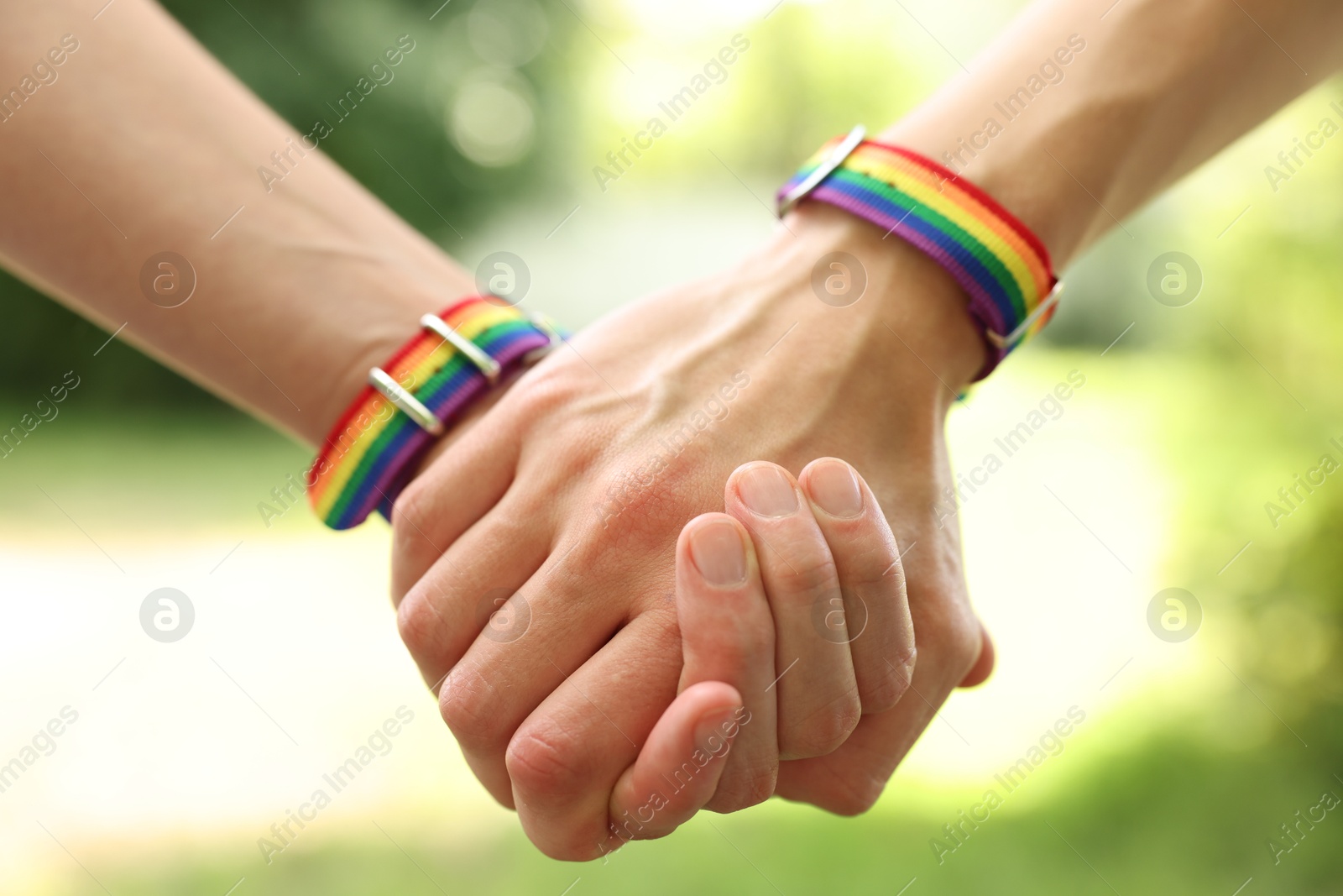 Photo of LGBT concept. Women in rainbow wristbands holding hands outdoors, closeup