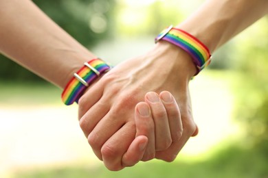 Photo of LGBT concept. Women in rainbow wristbands holding hands outdoors, closeup